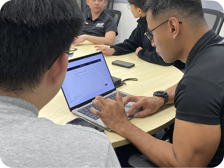 SCDF officers testing the Fynder loan request flow on a laptop, with a colleague pointing at the screen